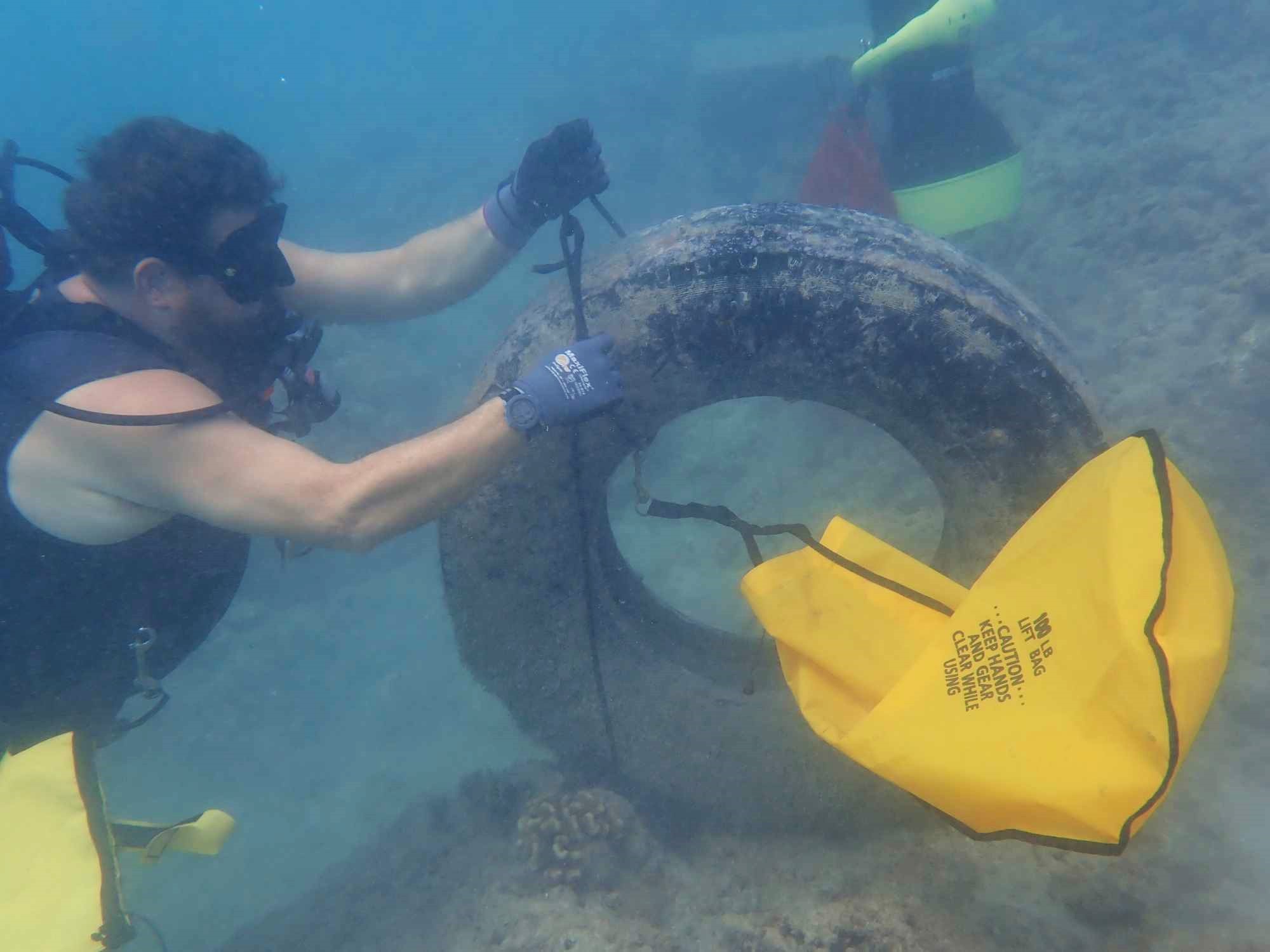 Nudi Wear volunteer Jim Sowa using a lift bag to remove a tire from the ocean in Hawaii