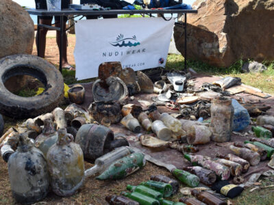 Trash pulled from the sea has been lined up in front of Nudi Wear's banner. There are items like bottles, tires, and plastic utensils. Sometimes ghost fishing gear turns up during these cleanups.