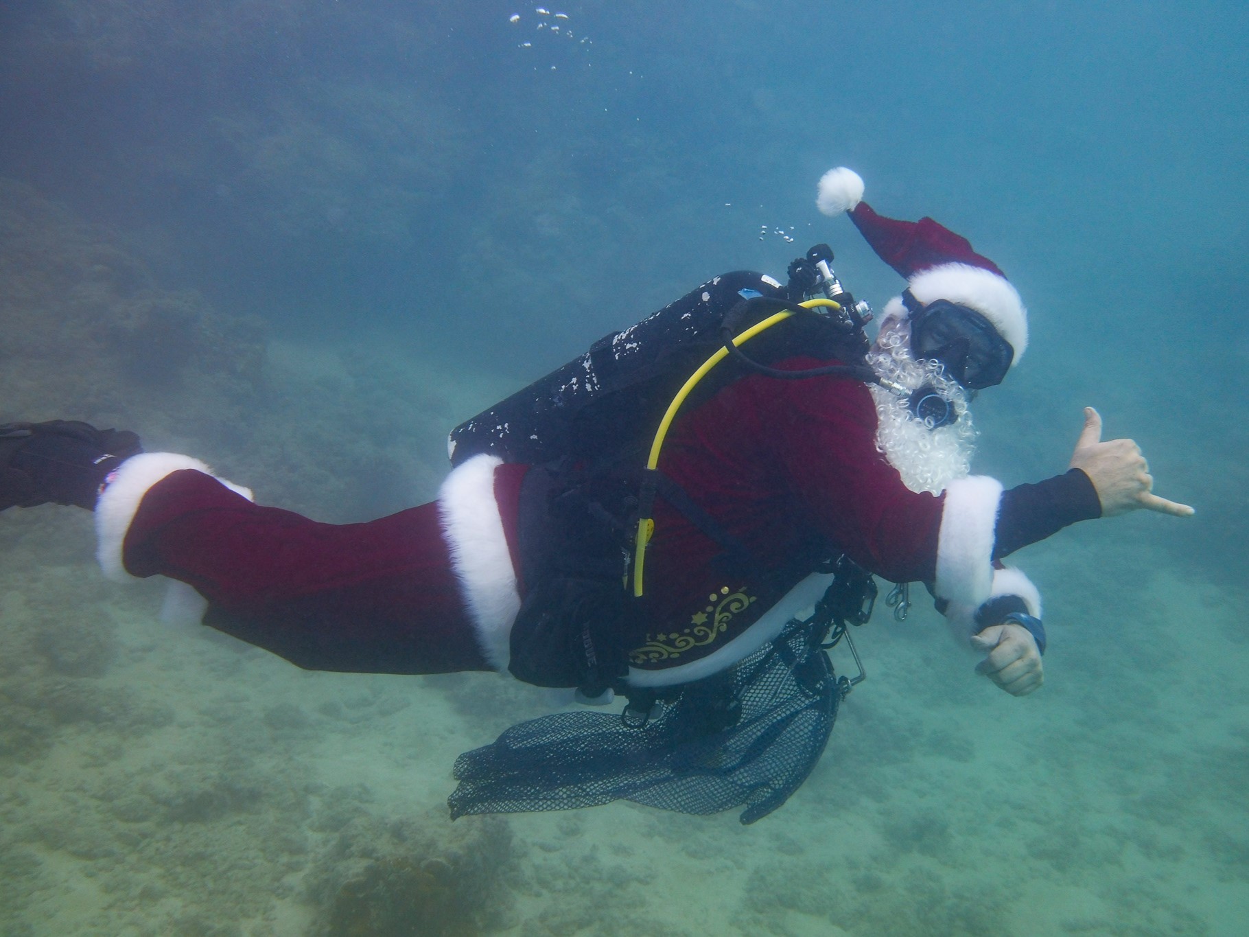 Santa scuba diving and giving a shaka sign with his right hand