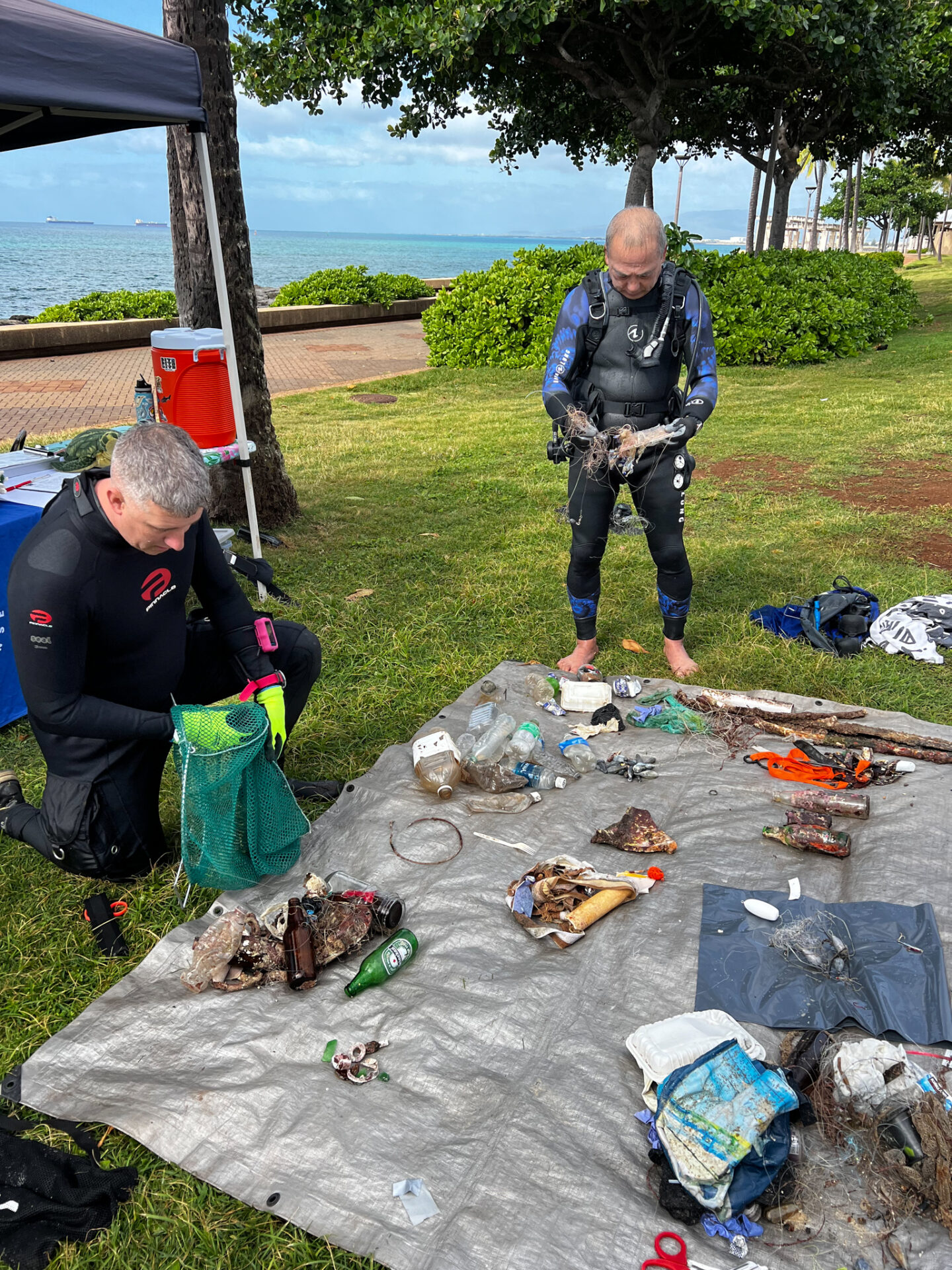 Volunteer divers sorting through trash in mesh bags during a Nudi Wear cleanup at Point Panic