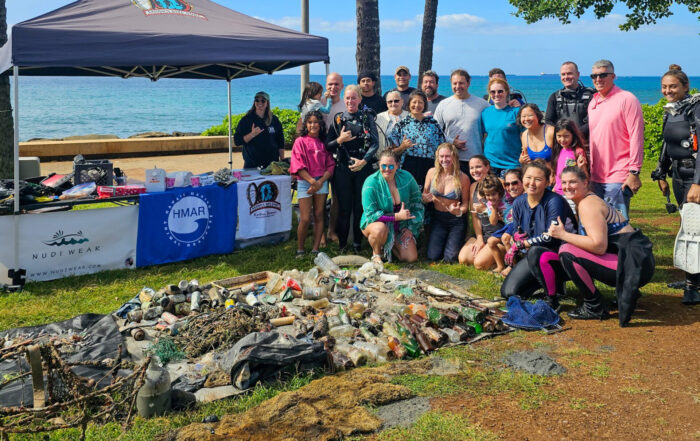 Volunteers from Nudi Wear, Aaron's Dive Shop, and HMAR posing behind 237 pounds of trash removed from the ocean during a cleanup at Point Panic Beach Park January 13th, 2024