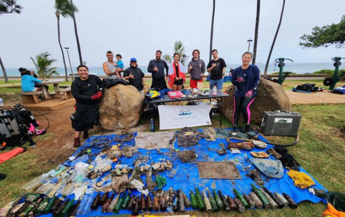 Nudi Wear volunteer divers at Point Panic Beach Park posing with a blue tarp covered with marine debris they removed from the ocean