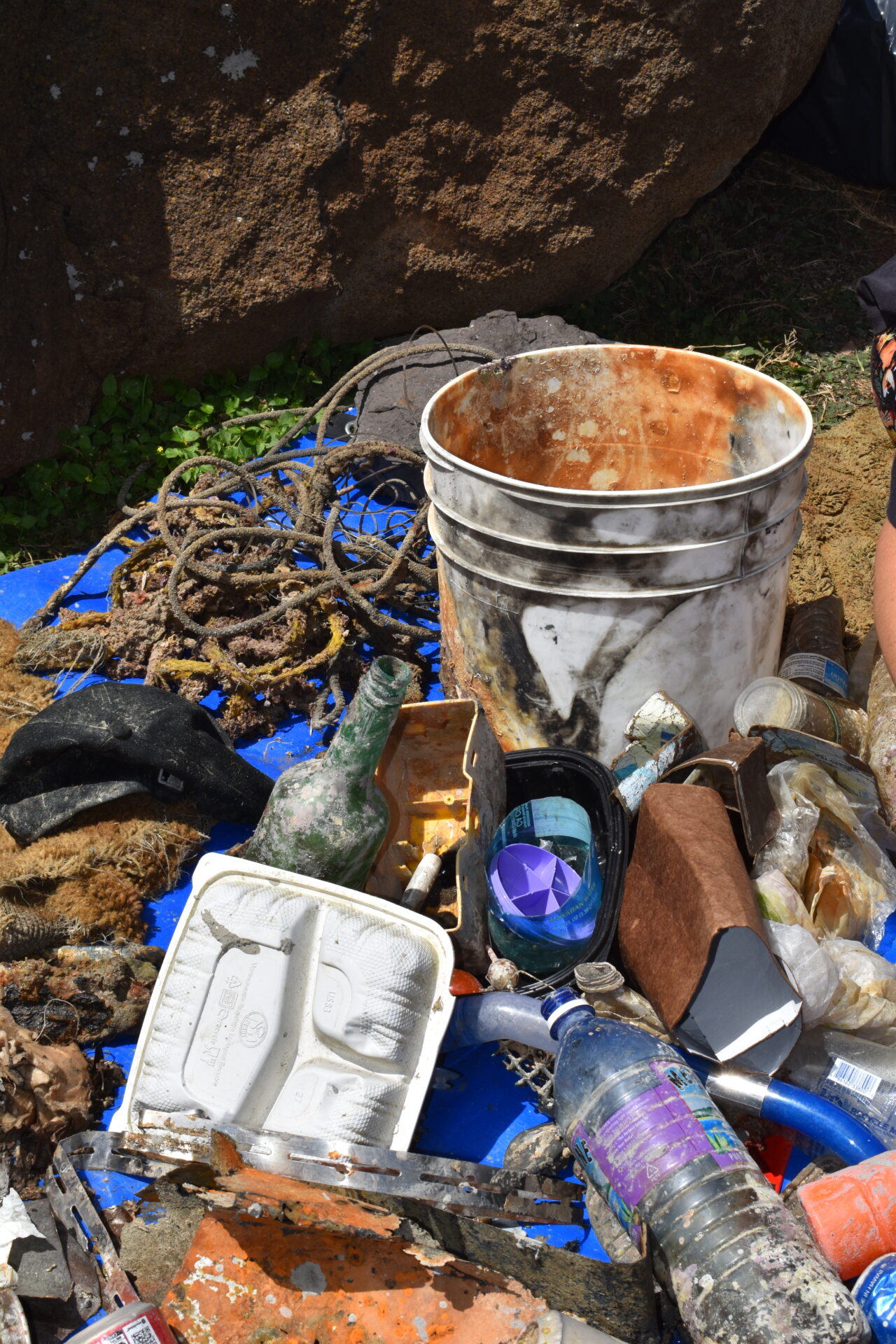 A large pile of trash including a bucket and single use plastics that was removed from the ocean during a Nudi Wear cleanup dive at Point Panic