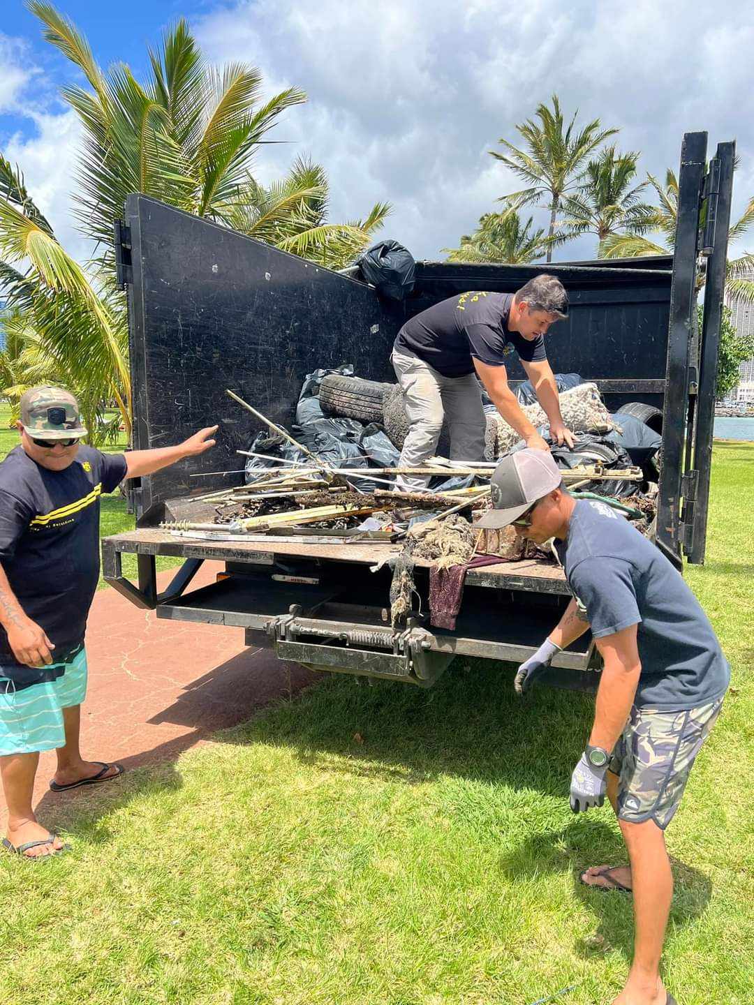 Volunteers tossing trash into Aloha Junk Man's truck on Magic Island during the Earth Day Hawaii cleanup