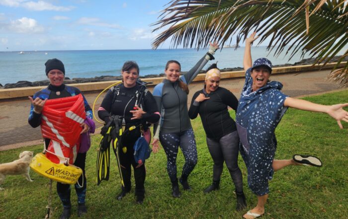A group of female volunteer divers from the Nudi Wear, Aaron's Dive Shop, and Ocean Alliance Project excited for the cleanup dive